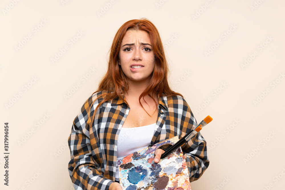 Teenager redhead girl holding a palette over isolated background having doubts and with confuse face expression Teenager redhead girl holding a palette over isolated background having doubts and with confuse face expression