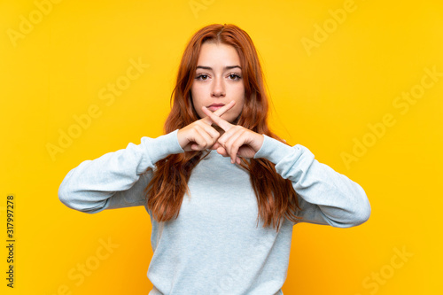 Teenager redhead girl over isolated yellow background showing a sign of silence gesture