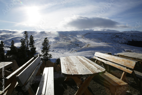  Empty wooden table in a cafe on the mountain in a snowstorm in the mountains in winter. Winter landscape. Panoramic view of the mountains.