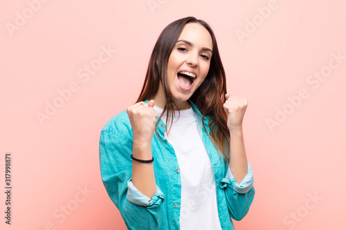 young pretty woman looking extremely happy and surprised, celebrating success, shouting and jumping against pink wall
