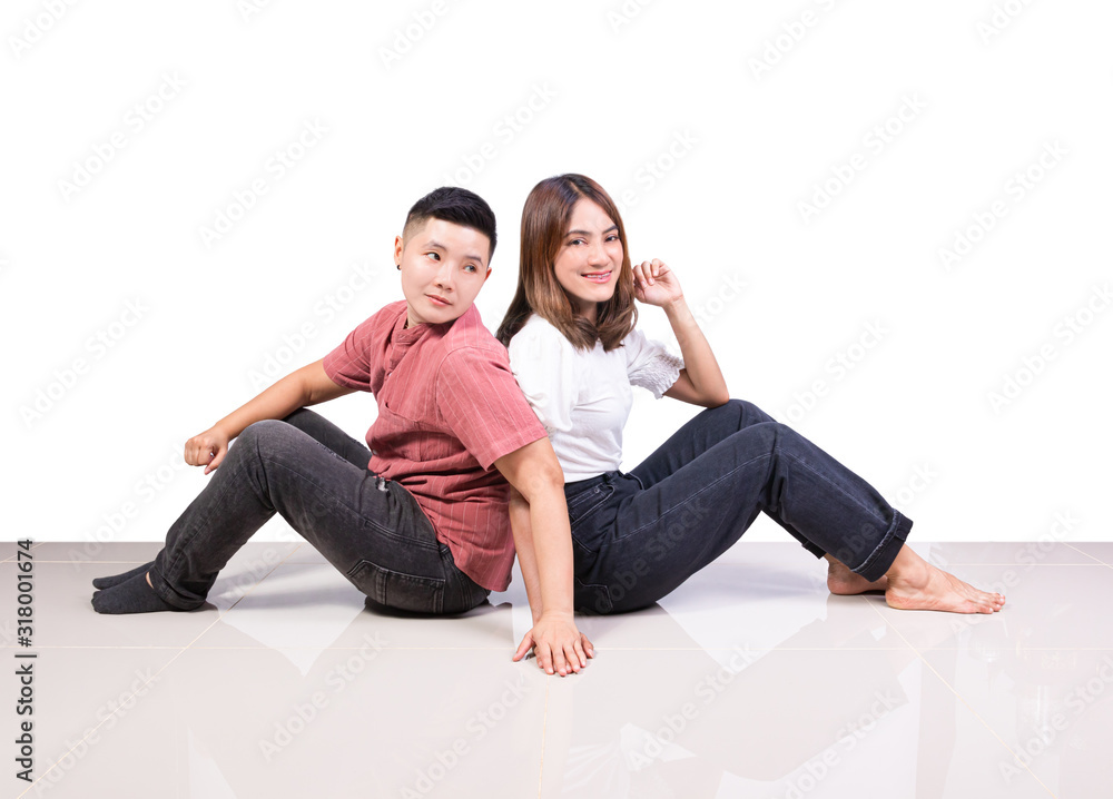 Two smiling woman young girls and happiness tomboy friends sitting back to back hold hand on tile floor in home with white background Two smiling woman young girls and happiness tomboy friends sitting back to back hold hand on tile floor in home with white background