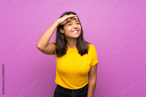 Young brunette girl over isolated background looking far away with hand to look something