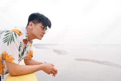 Side view portrait of young attractive Asian male wearing casual colorful shirt and sunglasses looking at the sea on his holiday. Travel inspirational and people lifestyle concept