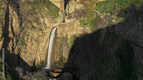 Gimbal shot of small waterfall under the stone bridge in Ronda city cliffs. Water stream under Ronda bridge and cliffs during sunset