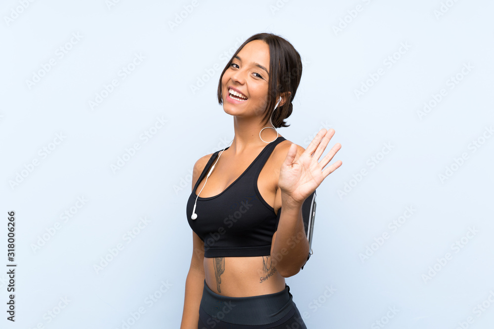 Young sport girl over isolated blue background saluting with hand with happy expression Young sport girl over isolated blue background saluting with hand with happy expression