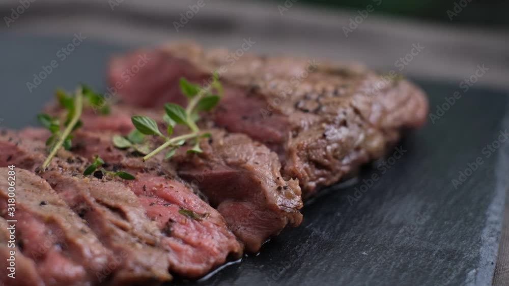 Grilled sliced beef steak medium rare with herbs and spices. set on black rustic stone board. Grilled sliced beef steak medium rare with herbs and spices. set on black rustic stone board.