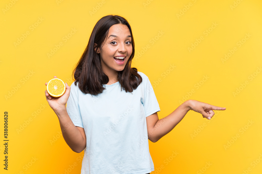 Young brunette woman holding an orange surprised and pointing finger to the side Young brunette woman holding an orange surprised and pointing finger to the side