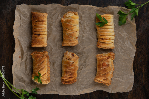 Baked puff pasrty with different fillings and herbs on baking paper or parchment on dark wooden background. Top view photo