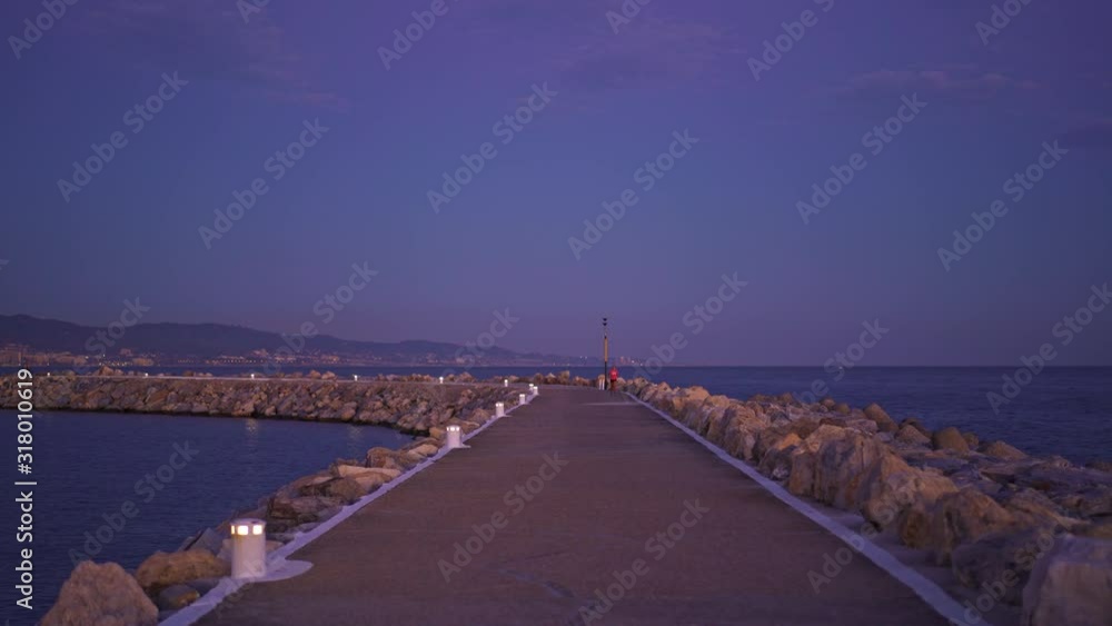 Handheld shot of the pier, asphalt road under evening stunning sunset sky in winter. Zoom in on pier of Puerto Banus Marbella in daylight with a runner Handheld shot of the pier, asphalt road under evening stunning sunset sky in winter. Zoom in on pier of Puerto Banus Marbella in daylight with a runner