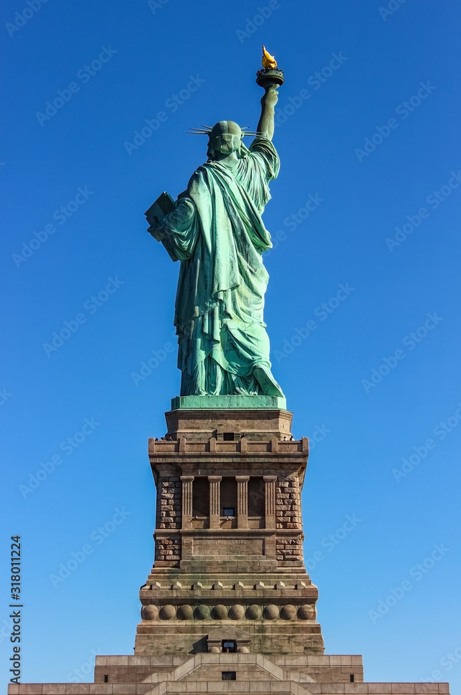 Fototapeta premium Statue of liberty seen from the back with a part of the pedestal on clear blue sky day, Liberty Island, New York, USA.