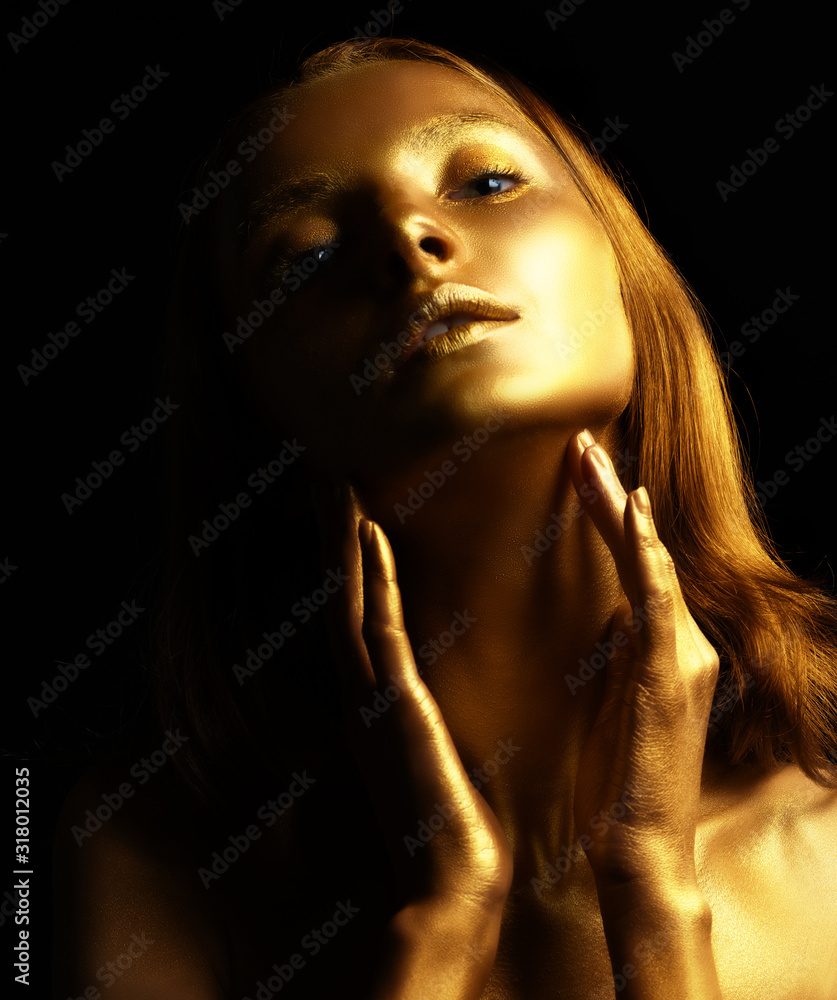 Golden woman lighted and shaded with graceful hands. Beauty fashion model girl with golden skin, makeup, hair black background. Fashion art portrait