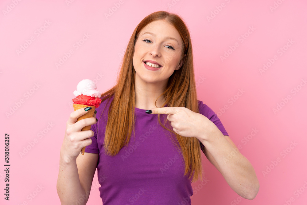Young redhead woman with a cornet ice cream over isolated pink background and pointing it Young redhead woman with a cornet ice cream over isolated pink background and pointing it