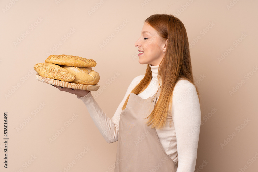 Young redhead woman in chef uniform. Female baker holding a table with several breads with happy expression Young redhead woman in chef uniform. Female baker holding a table with several breads with happy expression