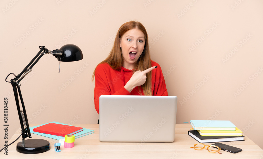 Young student woman in a workplace with a laptop surprised and pointing side Young student woman in a workplace with a laptop surprised and pointing side