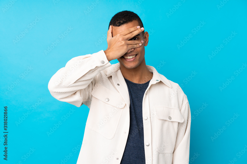 Young African American man over isolated blue background covering eyes by hands and smiling Young African American man over isolated blue background covering eyes by hands and smiling