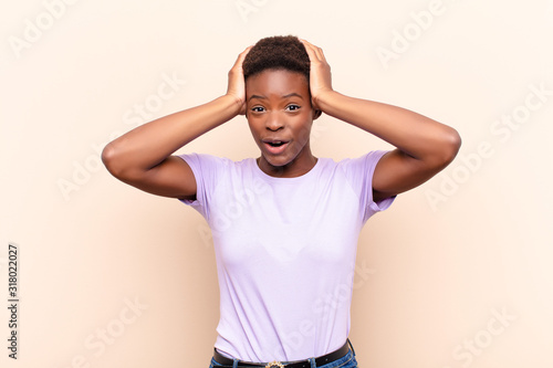 young pretty black womanlooking excited and surprised, open-mouthed with both hands on head, feeling like a lucky winner photo