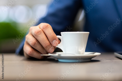 Businessman in a blue jacket with a cup of coffee in the cafe at the table  closeup