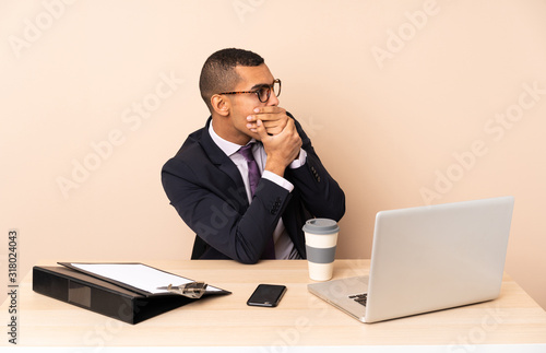 Young business man in his office with a laptop and other documents covering mouth and looking to the side © luismolinero