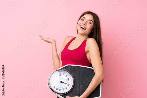 Pretty young girl with weighing machine over isolated pink background with weighing machine