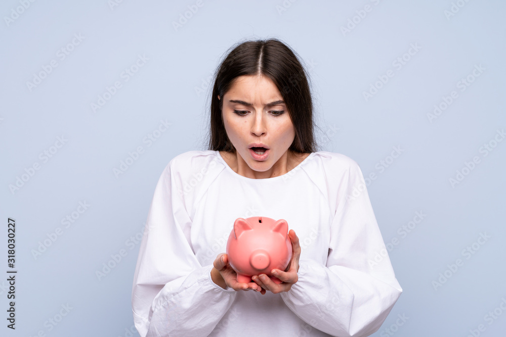 Young woman over isolated blue background holding a big piggybank Young woman over isolated blue background holding a big piggybank