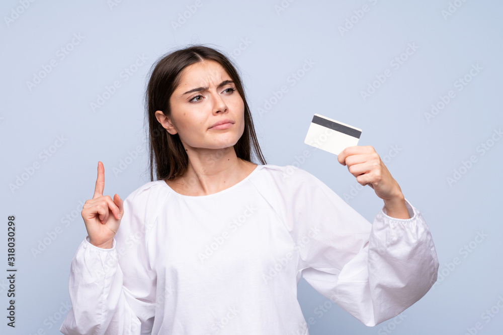 Young woman over isolated blue background holding a credit card Young woman over isolated blue background holding a credit card
