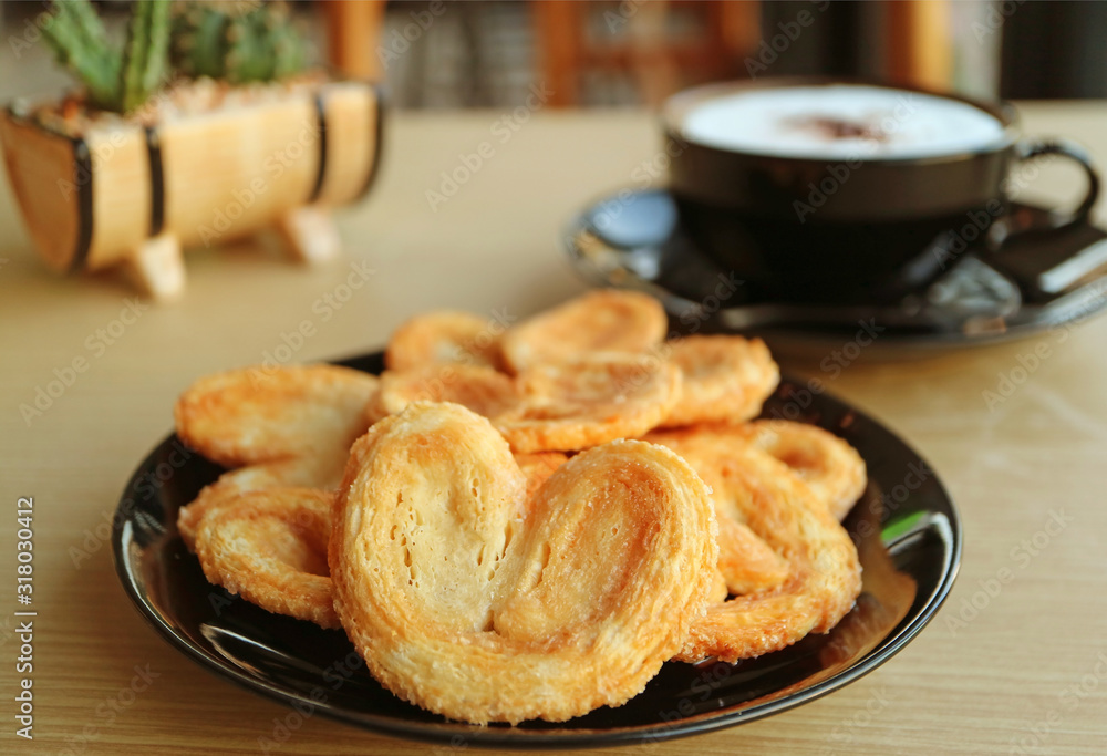 Closeup a Plate of French Palmier Pastries with Blurry Cappuccino and Potted Plants in Background Closeup a Plate of French Palmier Pastries with Blurry Cappuccino and Potted Plants in Background