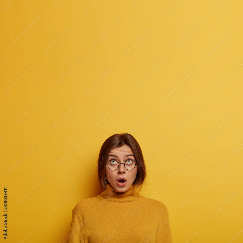 Φωτογραφία Vertical shot of emotional European woman concentrated above, gasps from fear an