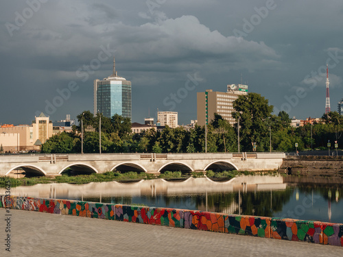 Bild auf Leinwand City view with a buildings on the background and river and bridge at the foregro