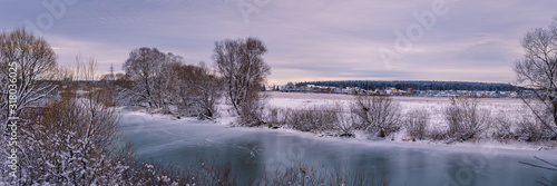 Panoramic view of a winter river with snowy banks and ice.