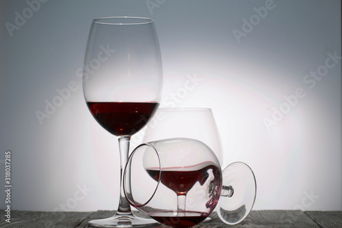 Glasses with red dry wine. One of them lies on its side with the remains of wine. Stand on wooden boards. Shot in backlight.