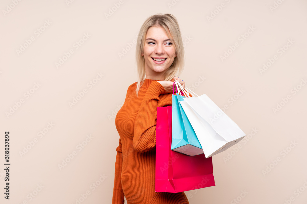 Young blonde woman over isolated background holding shopping bags and looking back