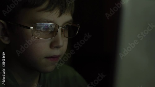 A boy with glasses plays a game on a computer.