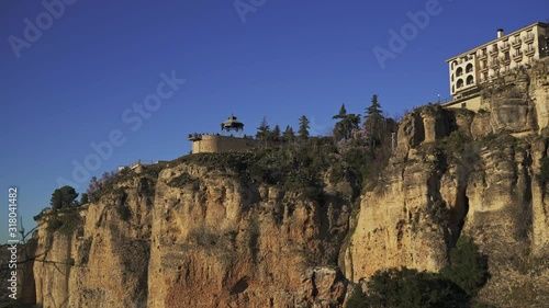 Pan shot left to right of stone bridge in Ronda city cliffs and old stone houses. Water stream under Ronda bridge and cliffs, evening sun
