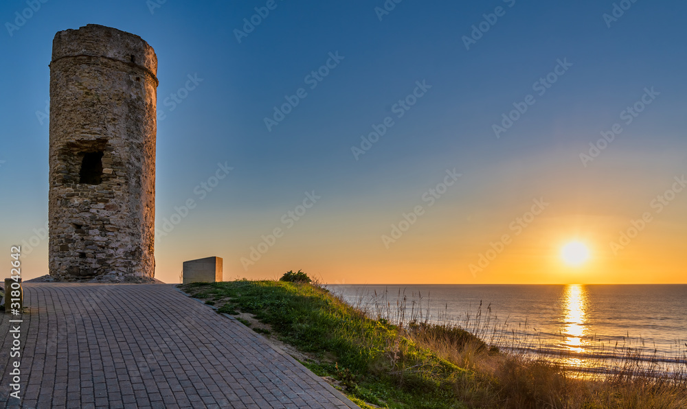 Serene ocean sunset near Torre del Puerco, a historic watch tower in Chiclana de la Frontera, Cadiz, Spain.