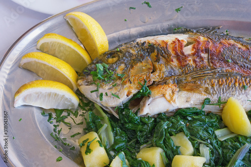 Balkan cuisine. Grilled fish ( sea bream ) with green leafy vegetables and slices of lemon photo