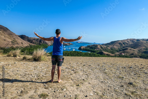 A man standing on top of the Komodo Island in Indonesia. The man is having a lot of fun, enjoying her time. Happiness and fun while travelling. Discovering new places. There is a lot of boats photo