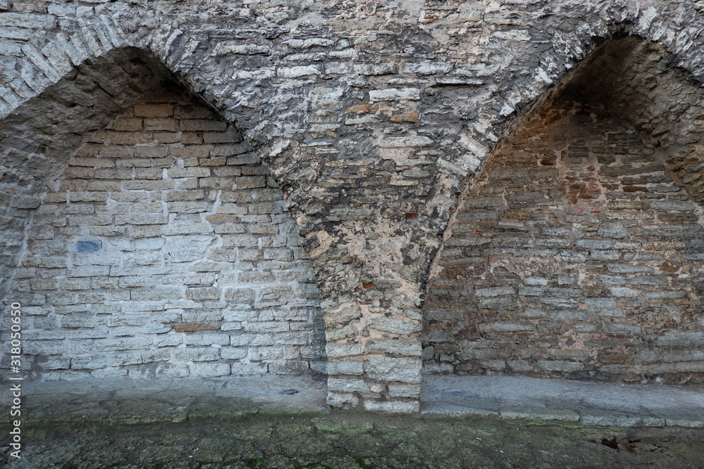 Fototapeta premium Niches in the form of arches in the old fortress wall. You can see the construction of the wall and arches of gray stone blocks. Background. Texture.