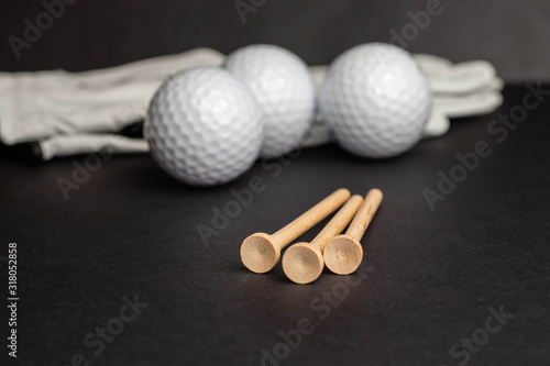Slika na platnu Golf ball tee’s in front of golf balls and gloves illustrative photo shot on black studio background isolated recreational sport equipment for golf courses and leisure, hobbies and retirement