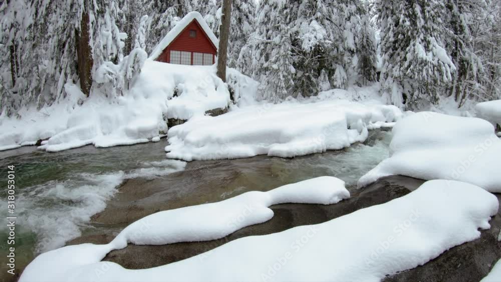 Red Cabin in the Woods Covered in Winter Snow by Flowing River Water Red Cabin in the Woods Covered in Winter Snow by Flowing River Water