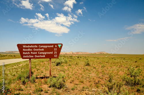 brown road sign indicating the distance to different destinations, in the background blue sky with white clouds.