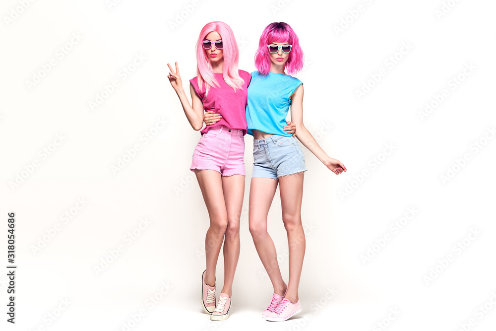 Two fashionable girl having fun in studio. Beautiful Excited young woman in Stylish summer colorful outfit, Trendy dyed pink hair. Glamour funny model sister, pink fashion hairstyle concept on white Two fashionable girl having fun in studio. Beautiful Excited young woman in Stylish summer colorful outfit, Trendy dyed pink hair. Glamour funny model sister, pink fashion hairstyle concept on white