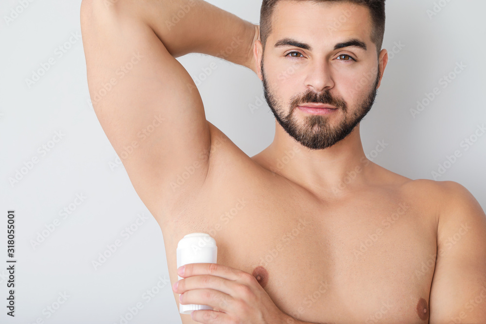 Fototapeta premium Handsome young man using deodorant on light background