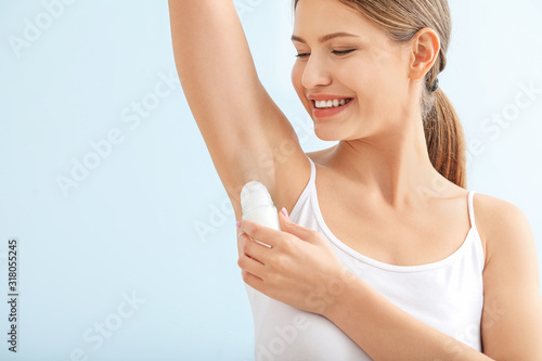 Beautiful young woman using deodorant on color background