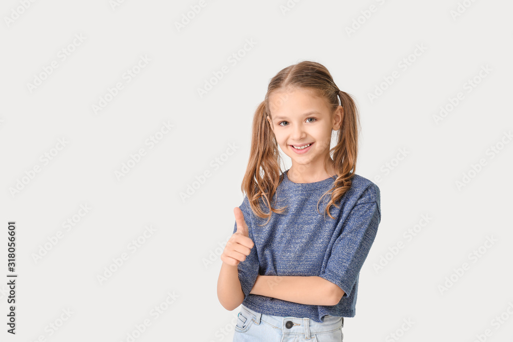 Fototapeta premium Cute little girl showing thumb-up gesture on white background