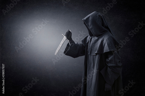 Hooded man with ancient knife in the dark