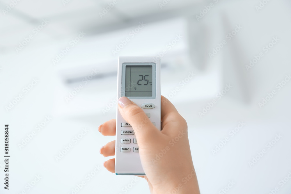 Young woman switching on air conditioner at home, closeup Young woman switching on air conditioner at home, closeup