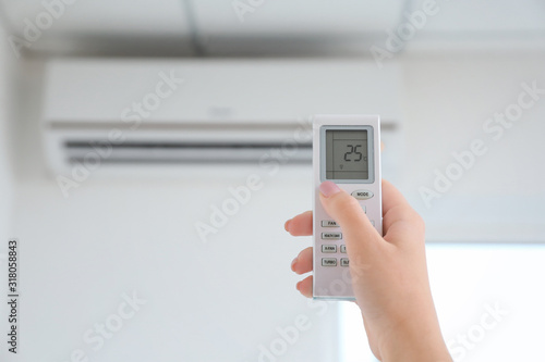 Young woman switching on air conditioner at home, closeup