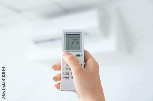 Young woman switching on air conditioner at home, closeup