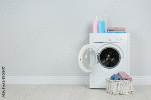 Modern washing machine with stack of towels, detergents and laundry basket near white wall, space for text