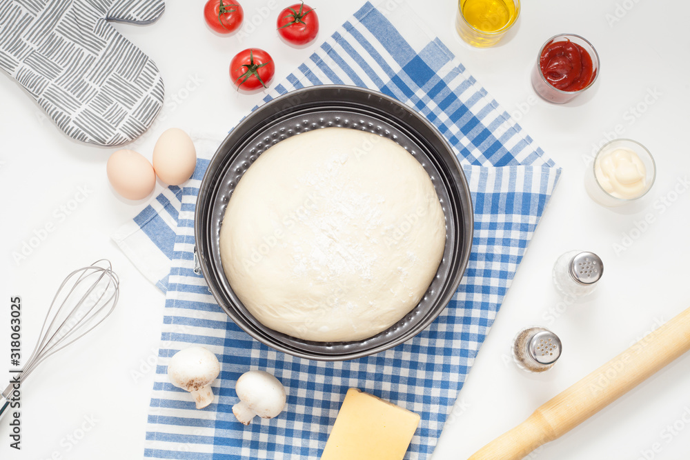 The dough is seen close-up from above, sprinkled with flour, on a table next to a rolling pin and eggs, appliances and ingredients for making pizza or pie. The concept of home cooking, baking. The dough is seen close-up from above, sprinkled with flour, on a table next to a rolling pin and eggs, appliances and ingredients for making pizza or pie. The concept of home cooking, baking.